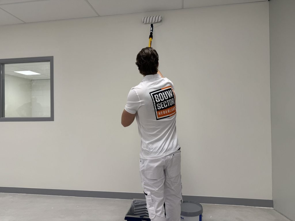 Schilder saust met een roller aan een verlengsteel een witte wand tot aan het plafond