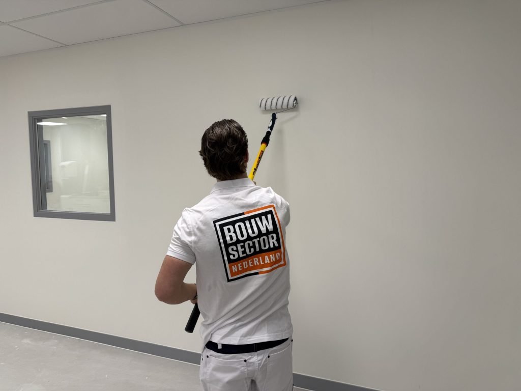 Schilder saust een lichte muur in een lege ruimte met een raam met grijs kozijn