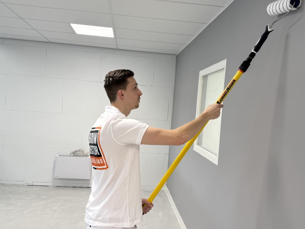 Schilder met lange roller werkt een grijze wand af in een lege ruimte met kalkzandsteen