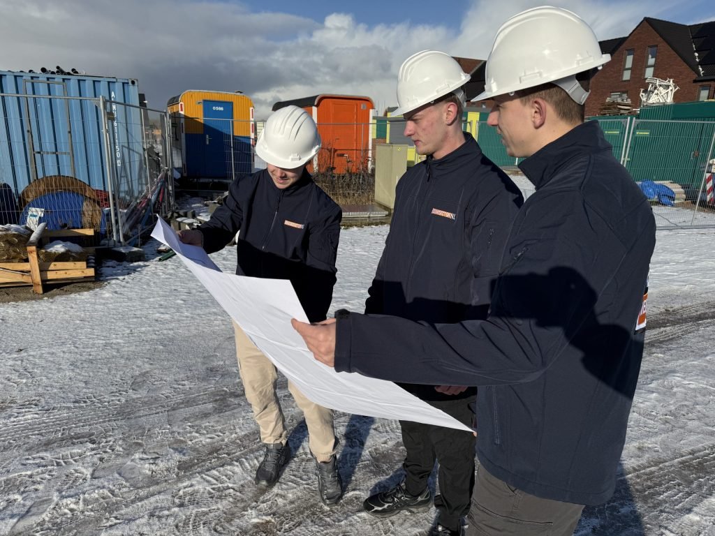 Drie vakmensen van Bouwsector Nederland met witte helm bekijken buiten een bouwtekening
